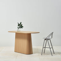 Light oak wood table with a smooth surface, paired with a sleek gray stool against a minimalist backdrop.