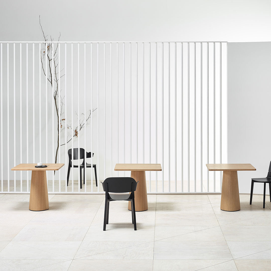Elegant wooden tables with natural oak finish and sleek black chairs against a minimalist white slatted backdrop.