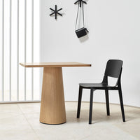 Wooden table with a light oak finish and sleek black chair against a minimalist white backdrop. Modern design elements.