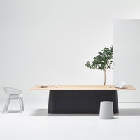 Modern minimalist desk featuring a light wood top and sleek black base, with a gray chair and accent pieces.