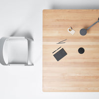 Light wood tabletop with subtle grain patterns, contrasting with a sleek gray chair and black stationary items.