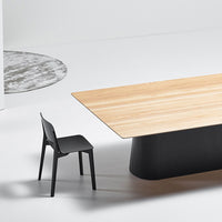 Modern black chair beside a sleek wooden table with light and dark wood patterns on a minimalistic backdrop.