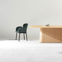 Green velvet chair with black legs beside a light wood table on a soft white carpet, creating a modern aesthetic.