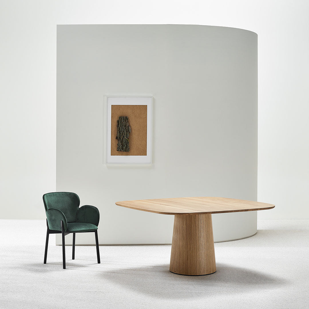 Green velvet chair and light oak table against a soft white background, featuring subtle earthy tones.