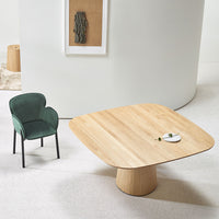 Natural oak table with smooth, light wood grain and a round, green velvet chair against a neutral backdrop.