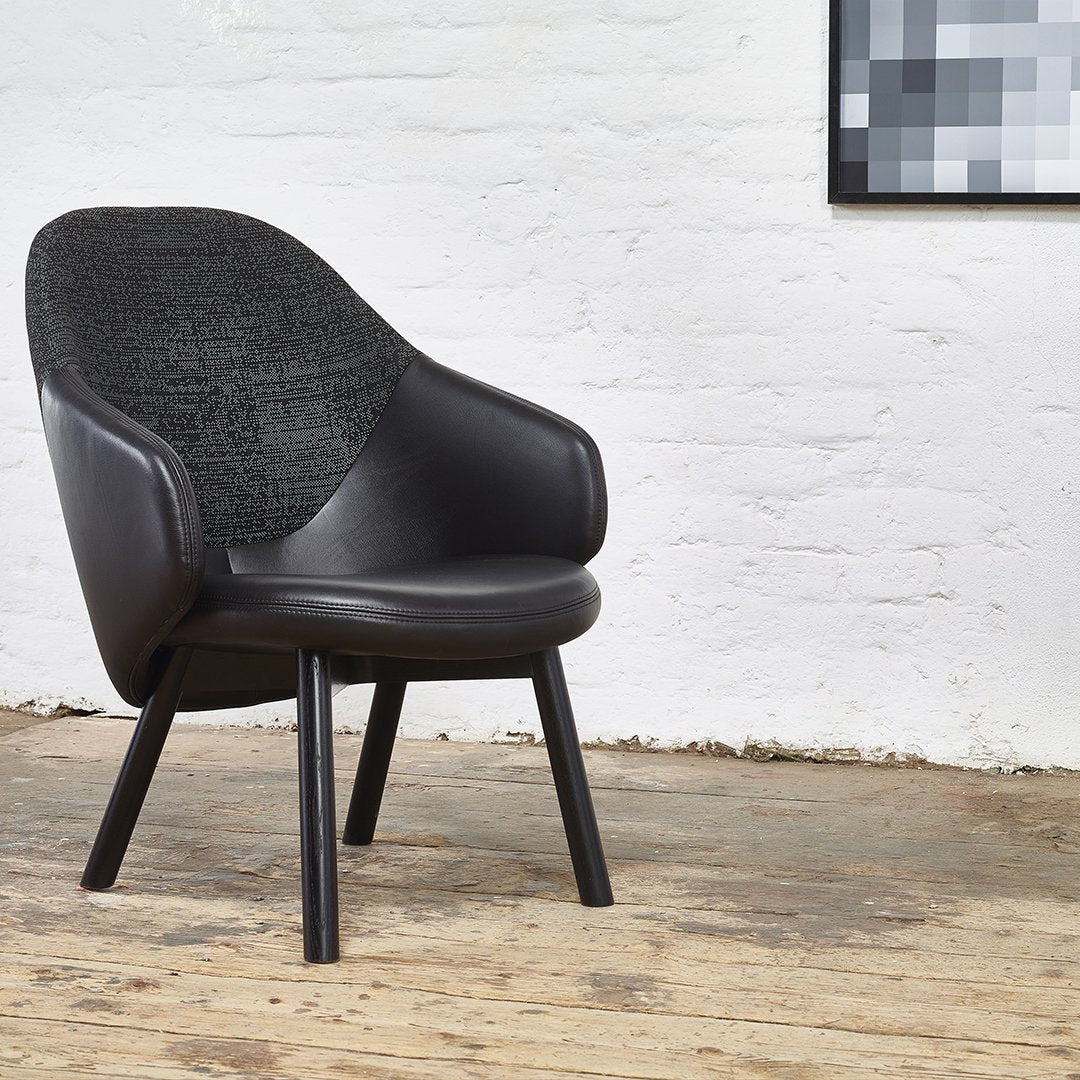 Black upholstered chair with textured grey backrest and sleek wooden legs against a rustic wooden floor.