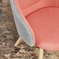 Pink and gray upholstered chair with a textured finish and natural wood legs, set against a rustic floor.