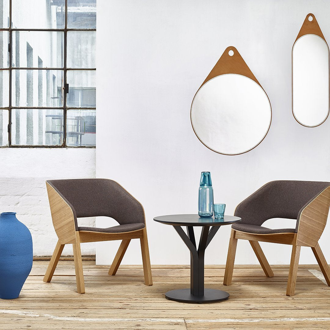 Stylish wooden chairs with gray fabric upholstery, blue vase, black table, and round mirrors on a white wall.