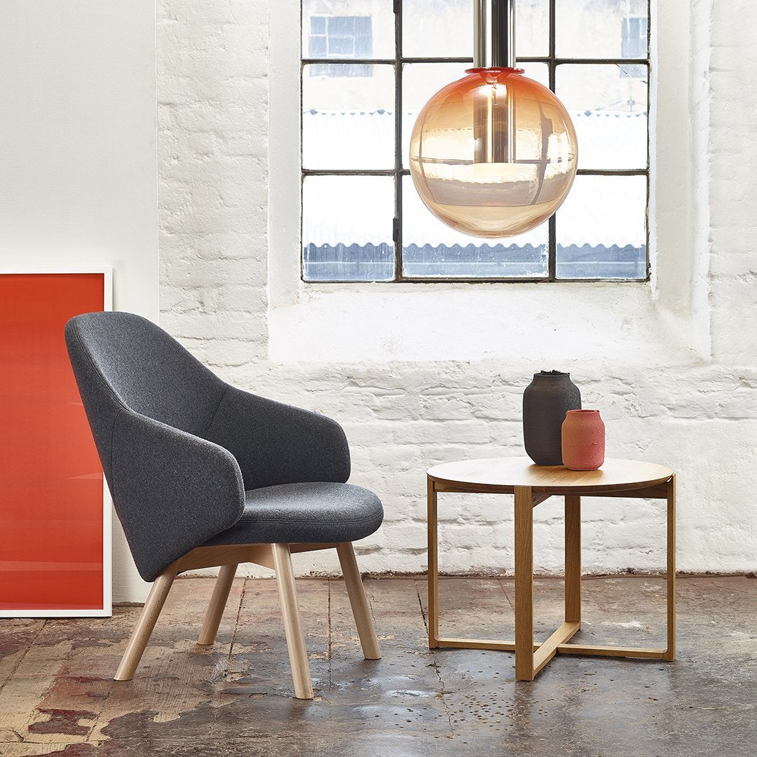 "Gray upholstered chair with wooden legs, gold pendant light, and colorful decor against a white brick wall."