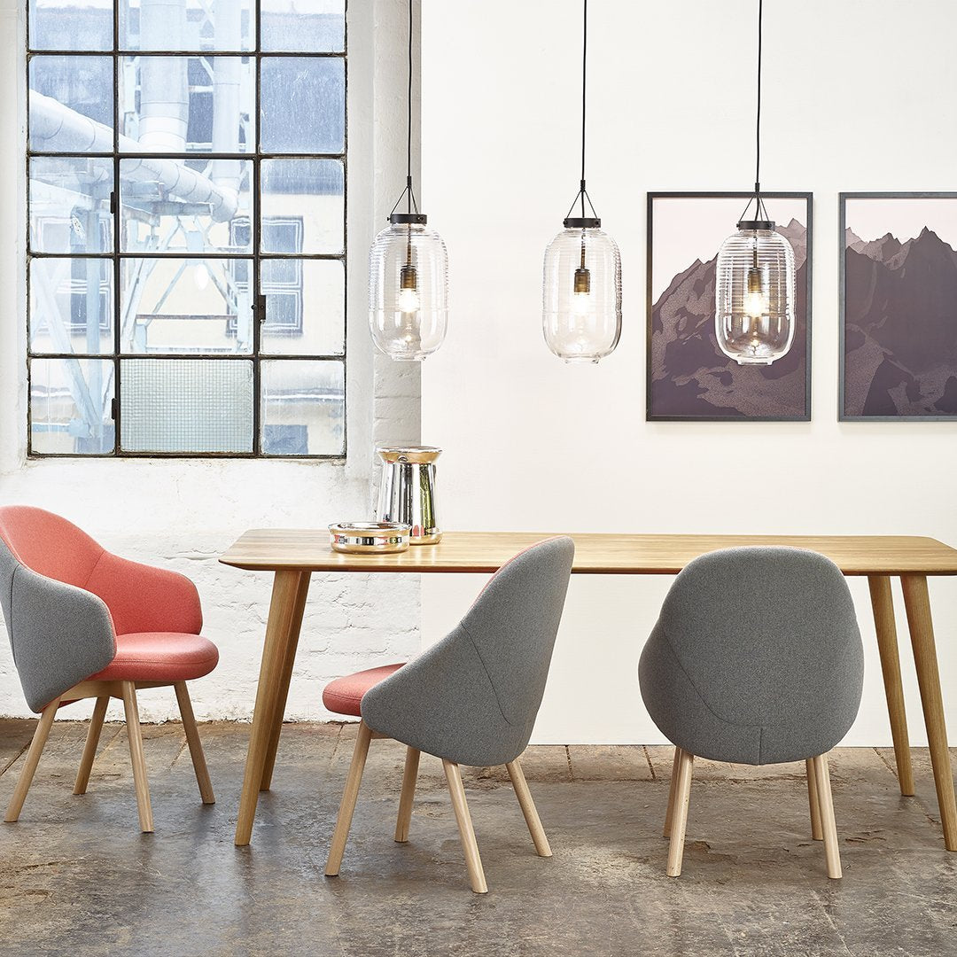 Modern dining room featuring pink and gray chairs, light wood table, and pendant lighting against a bright, airy backdrop.