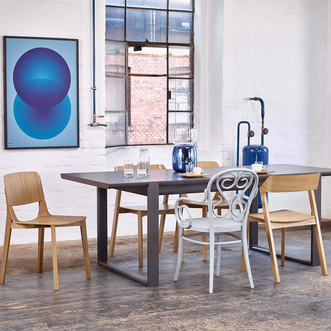 Modern dining set with a gray table, natural wood chairs, and a blue abstract wall art in a bright, minimalist space.
