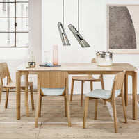 Light wood dining table with muted blue chair cushions, sleek metallic pendant lights, and neutral wall decor.