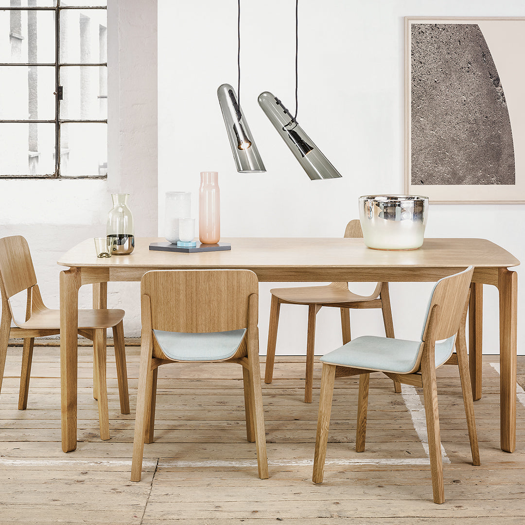 Light oak dining table with pastel blue chair cushions; modern minimalist decor with metallic pendant lights.