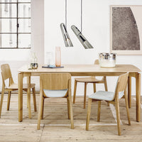 Light wooden dining table with light gray chairs, accented by sleek metallic pendant lights in a bright, airy setting.