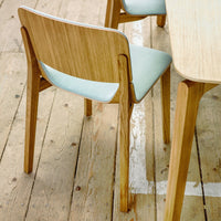Light wooden chair with a soft mint green cushion, minimalist design on a natural wood floor.