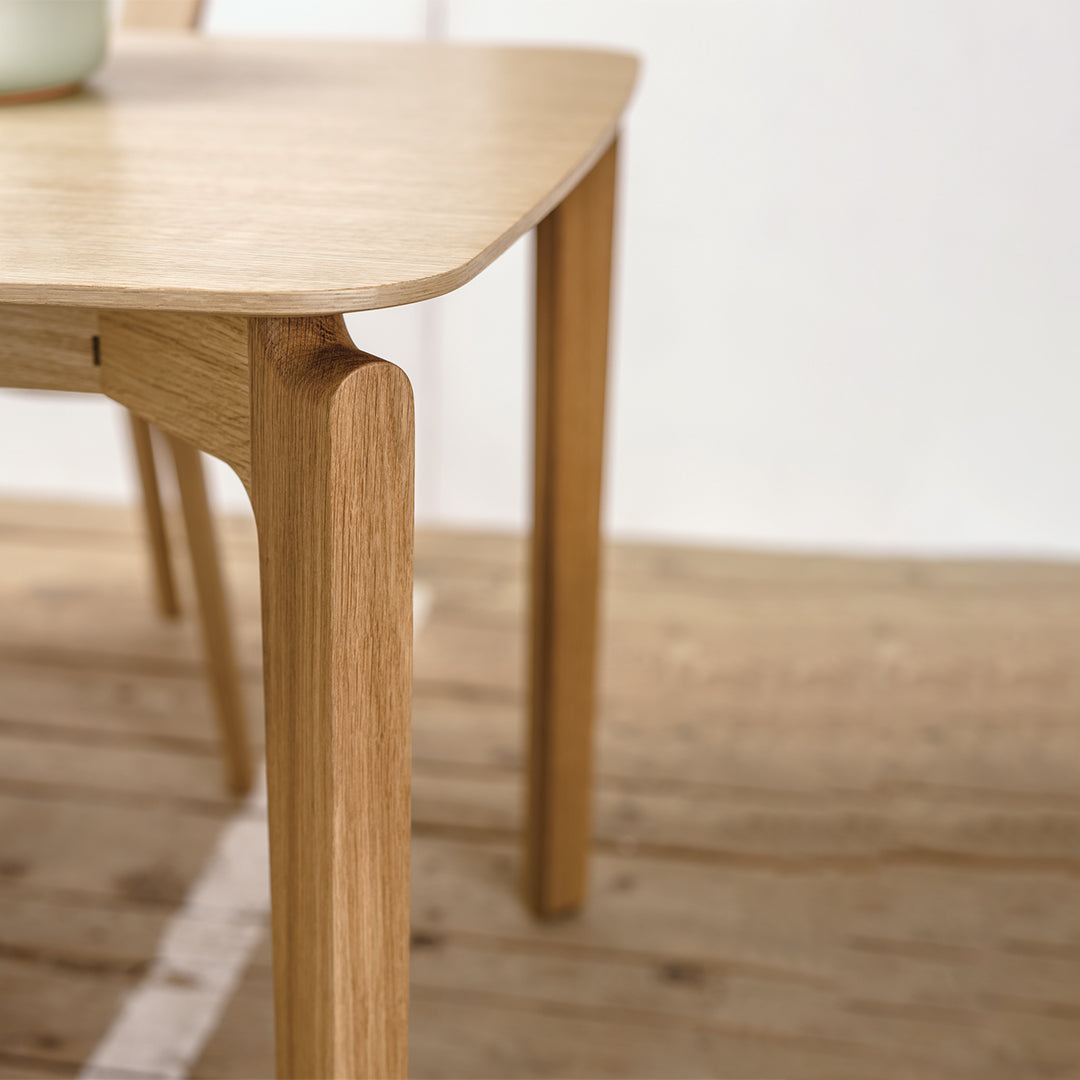 Natural wood dining table with a light finish and smooth, rounded edges on a rustic wooden floor.