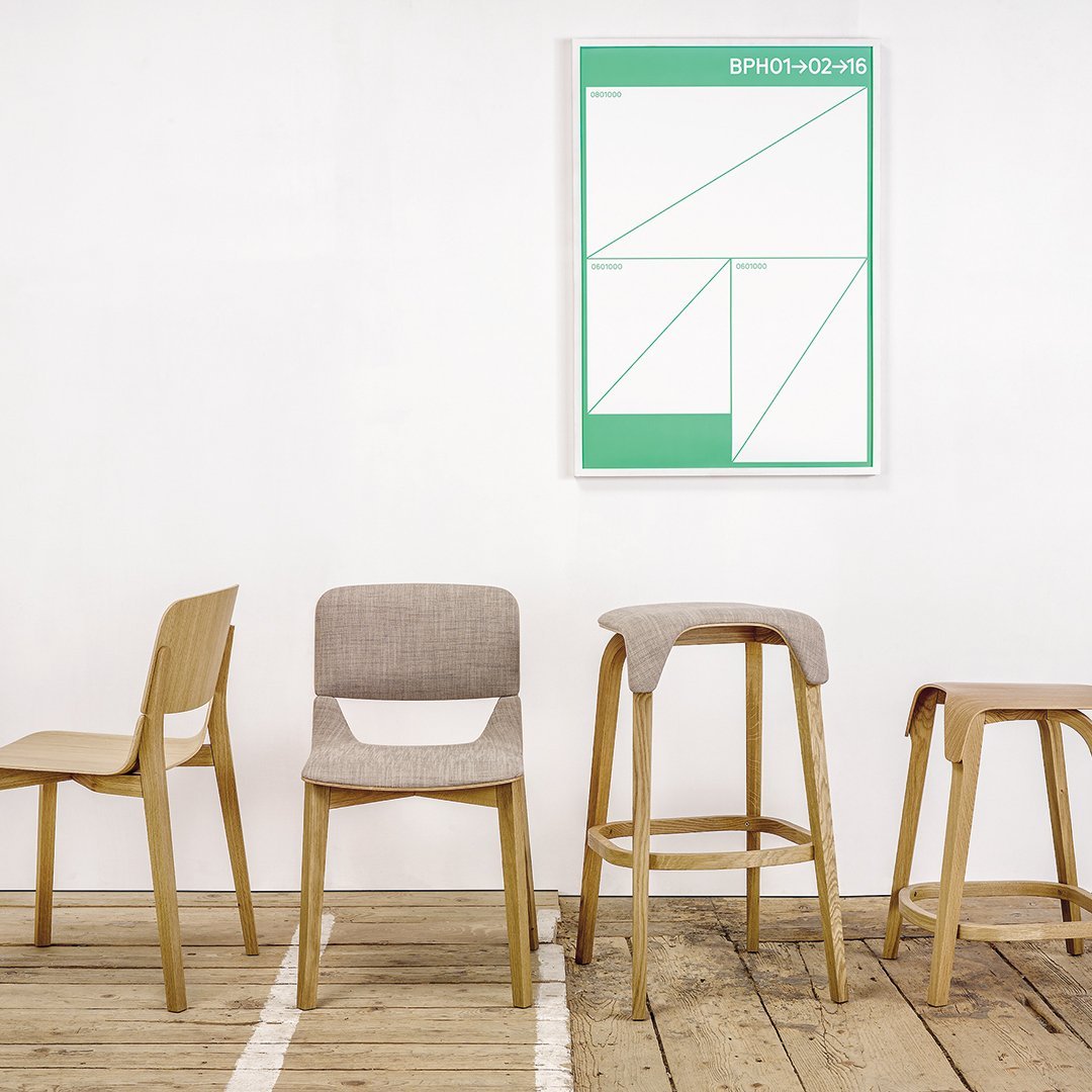 Four minimalist chairs in neutral tones, paired with a vibrant green geometric wall art, set against a wooden floor.