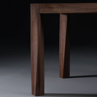 "Close-up of a walnut wooden table leg featuring rich brown tones and angular geometric patterns."