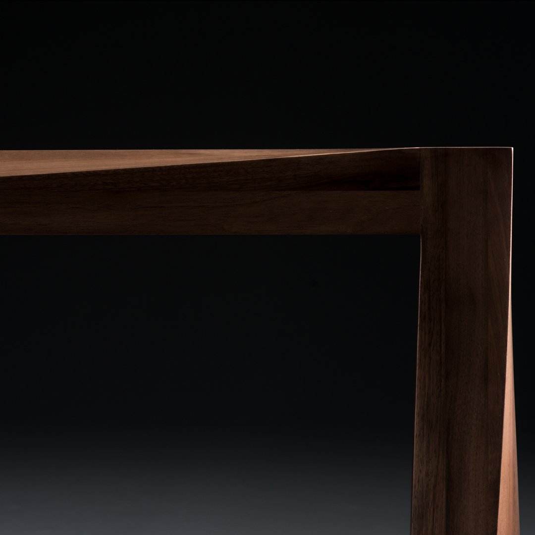 "Close-up of sleek dark wood table edge with a smooth finish against a black background."