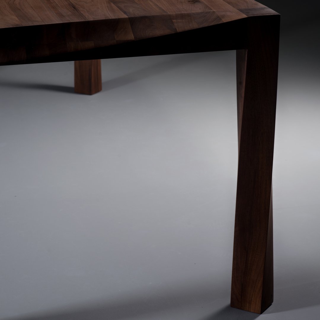 "Close-up of dark walnut wood table leg with sleek, angular design and rich, natural grain patterns."