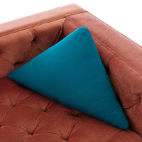 Teal triangle cushion on a rust-colored tufted sofa, creating a vibrant color contrast and modern look.