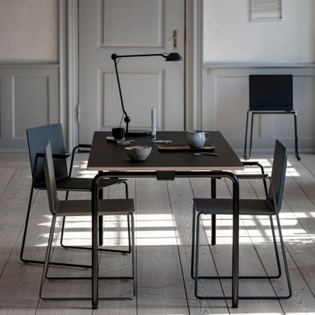 Modern black table with gray chairs and minimalistic decor, featuring clean lines and soft shadows on a wooden floor.