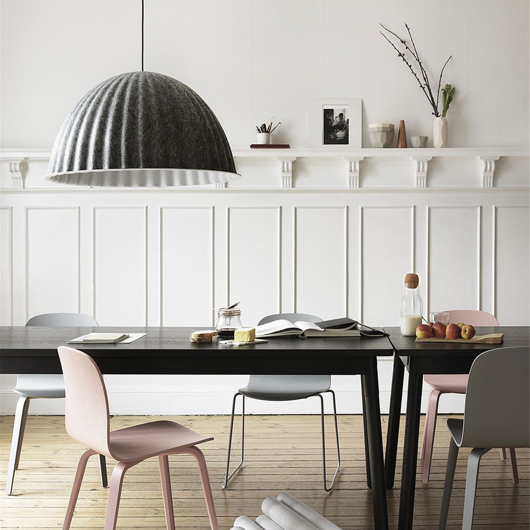 Modern dining scene with a sleek black table, pastel chairs in pink and gray, and a geometric gray pendant light.