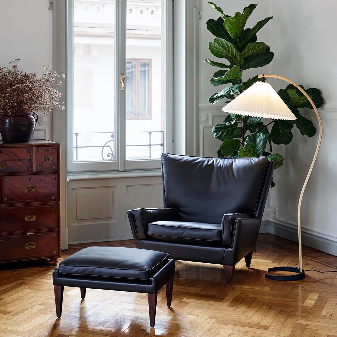 Black leather armchair with matching ottoman, set against a warm wood floor and neutral wall colors. Modern decor accents.