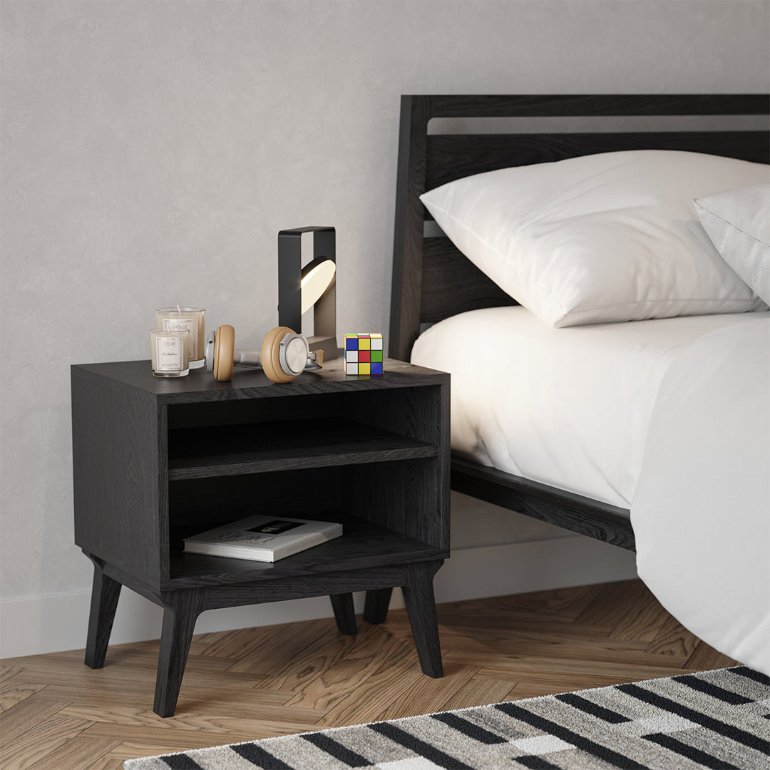 Black wooden nightstand with clean lines, paired with a striped black and white rug in a modern bedroom setting.