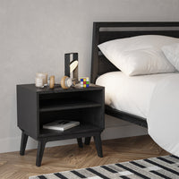 Black wooden nightstand with clean lines, paired with a striped black and white rug in a modern bedroom setting.