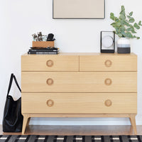 Natural wood dresser with light oak finish, featuring round handles and a black and white striped rug underneath.