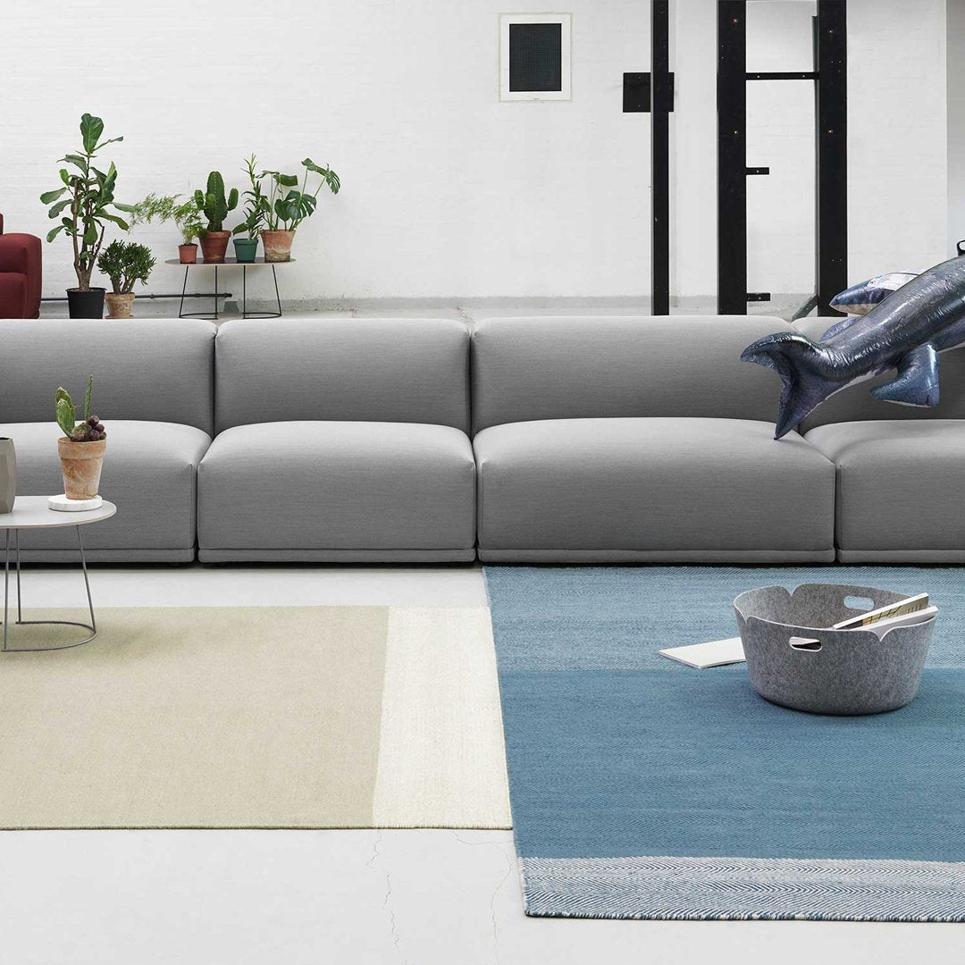 Modern gray sofa on a multicolored rug with beige, blue, and cream patterns. Green plants in the background.