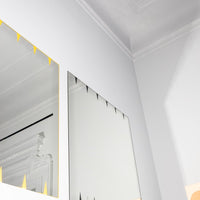 Mirrors featuring a sleek silver finish with bold yellow triangular accents against a minimalist white wall.