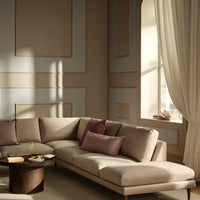 Modern beige sectional sofa with plum accent pillows, set against softly patterned cream walls and sheer beige curtains.