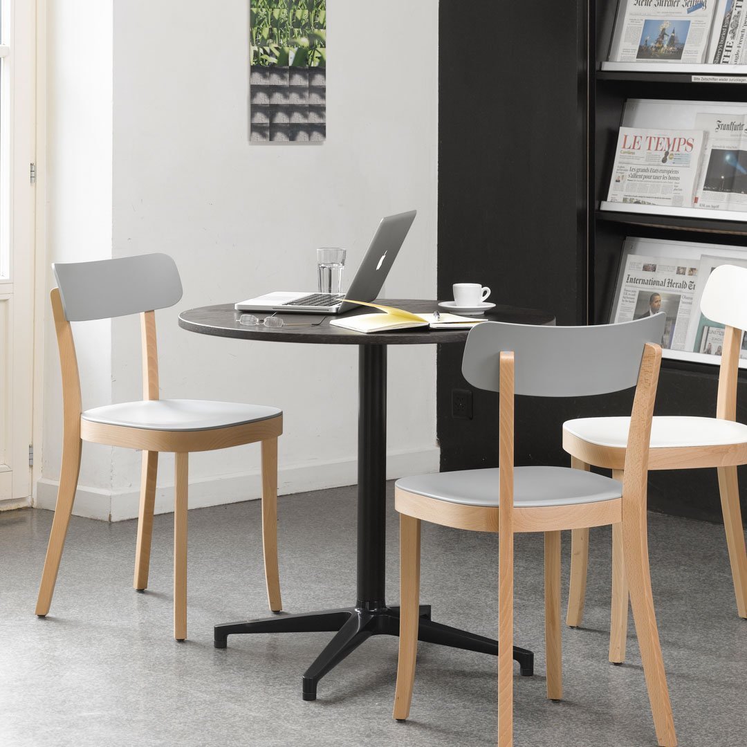 Modern round table with a black base, paired with light gray and natural wood dining chairs in a sleek design.