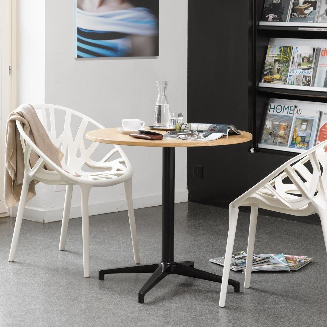 Modern round table with a light wood top and black metal base, surrounded by white patterned chairs. Perfect for stylish spaces.