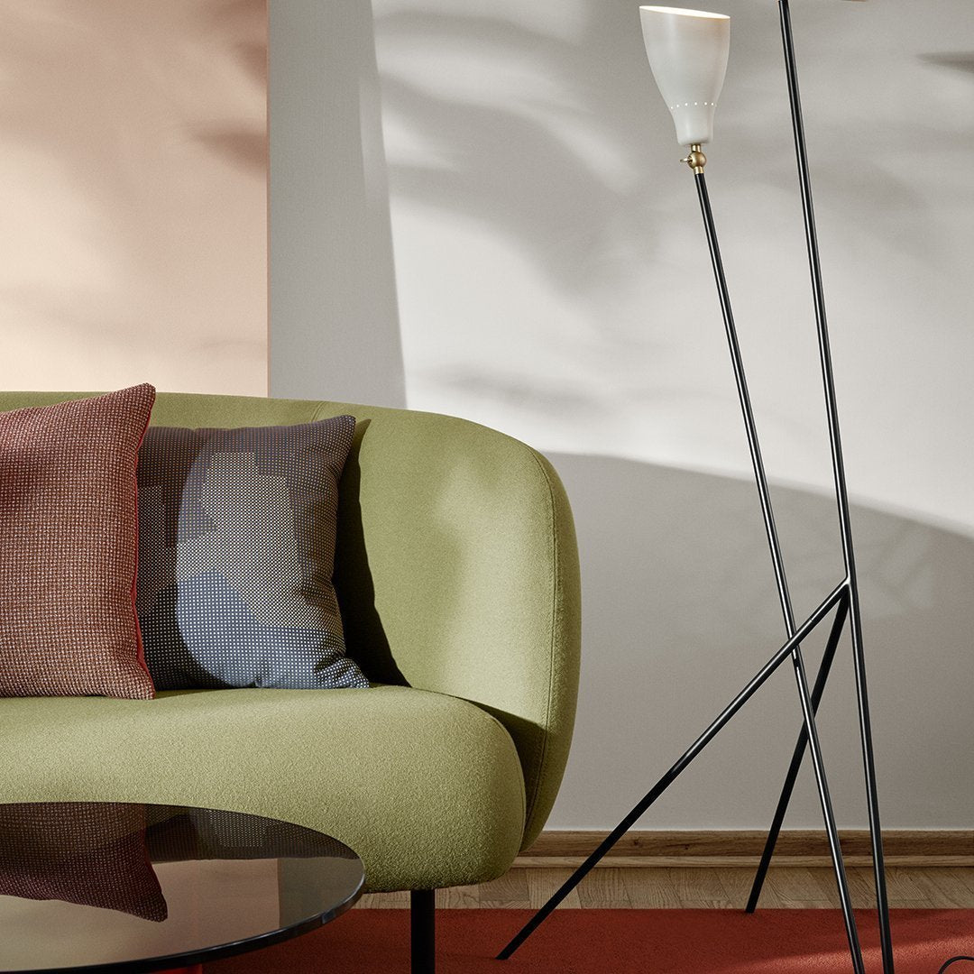 Green curved sofa with patterned pillows in shades of gray, purple, and maroon, set against a warm-toned backdrop.
