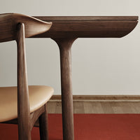 Modern wooden table with a dark finish, paired with a light tan seat on a vibrant red rug.