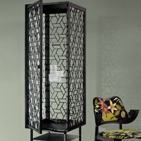 Black geometric patterned storage unit with vibrant floral chair in the foreground, set against a muted green wall.