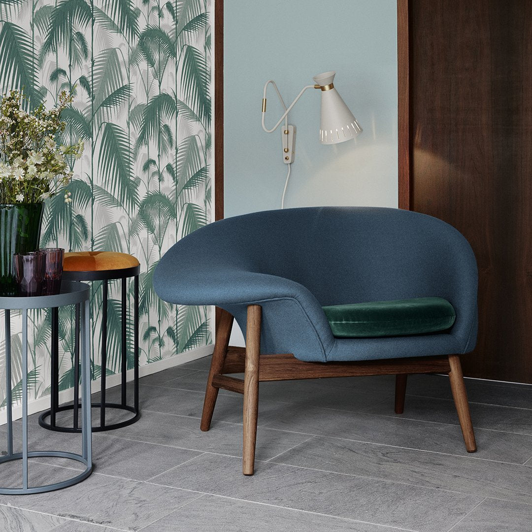 Blue upholstered chair with green accent cushion, set against a tropical leaf patterned wallpaper and neutral tones.