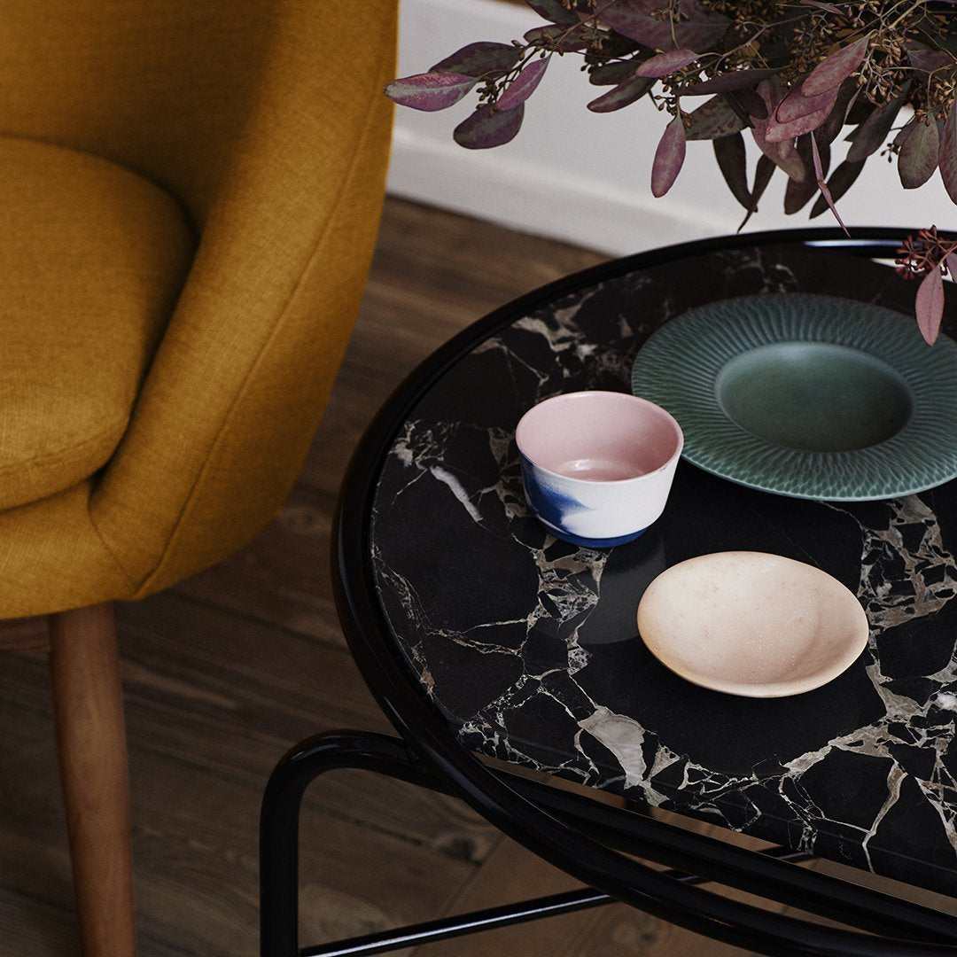 Black marble table with colorful ceramic dishes: soft pink, green, and minimalist white, alongside a mustard yellow chair.