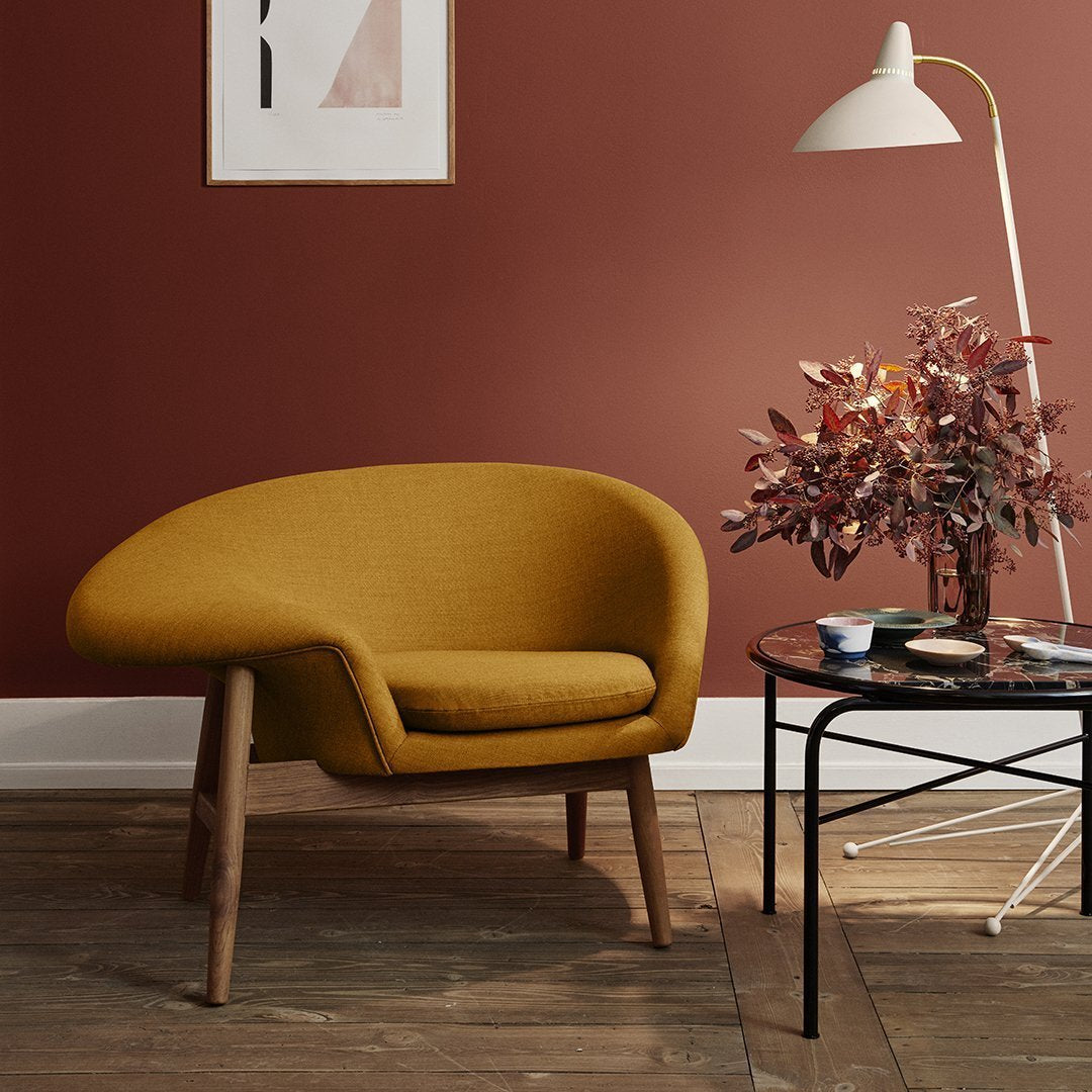 "Mustard yellow accent chair with a smooth, curved design against a deep earthy red wall, complemented by natural wood tones."