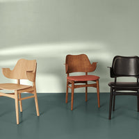 Three stylish chairs: natural wood, warm brown, and sleek black against a mint green backdrop and teal floor.