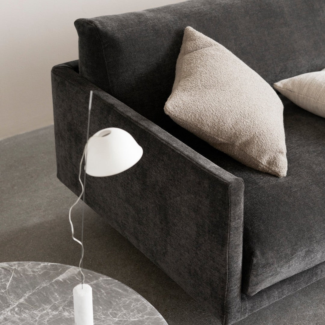 Soft gray sofa with textured charcoal fabric and beige accent pillows, complemented by a minimalist white lamp and marble table.