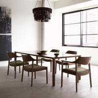 Modern wooden dining table with six green upholstered chairs in a minimalist, neutral-toned room with natural light.