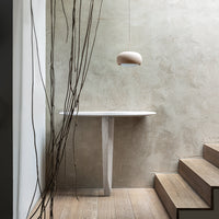 Modern white table with light wood legs against a textured gray wall and natural wood flooring. Simple, elegant design.