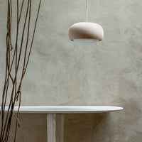 Soft beige pendant light against a textured taupe wall, complemented by a minimalist white table and delicate brown branches.