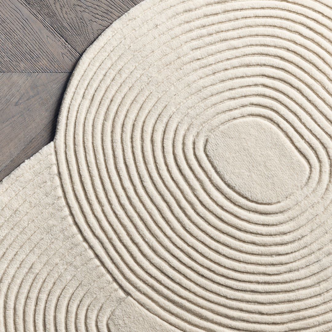 Beige circular rug with concentric spiral patterns on a wooden floor. Elegant design for modern interiors.