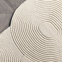 Beige circular rug with concentric spiral patterns on a wooden floor. Elegant design for modern interiors.