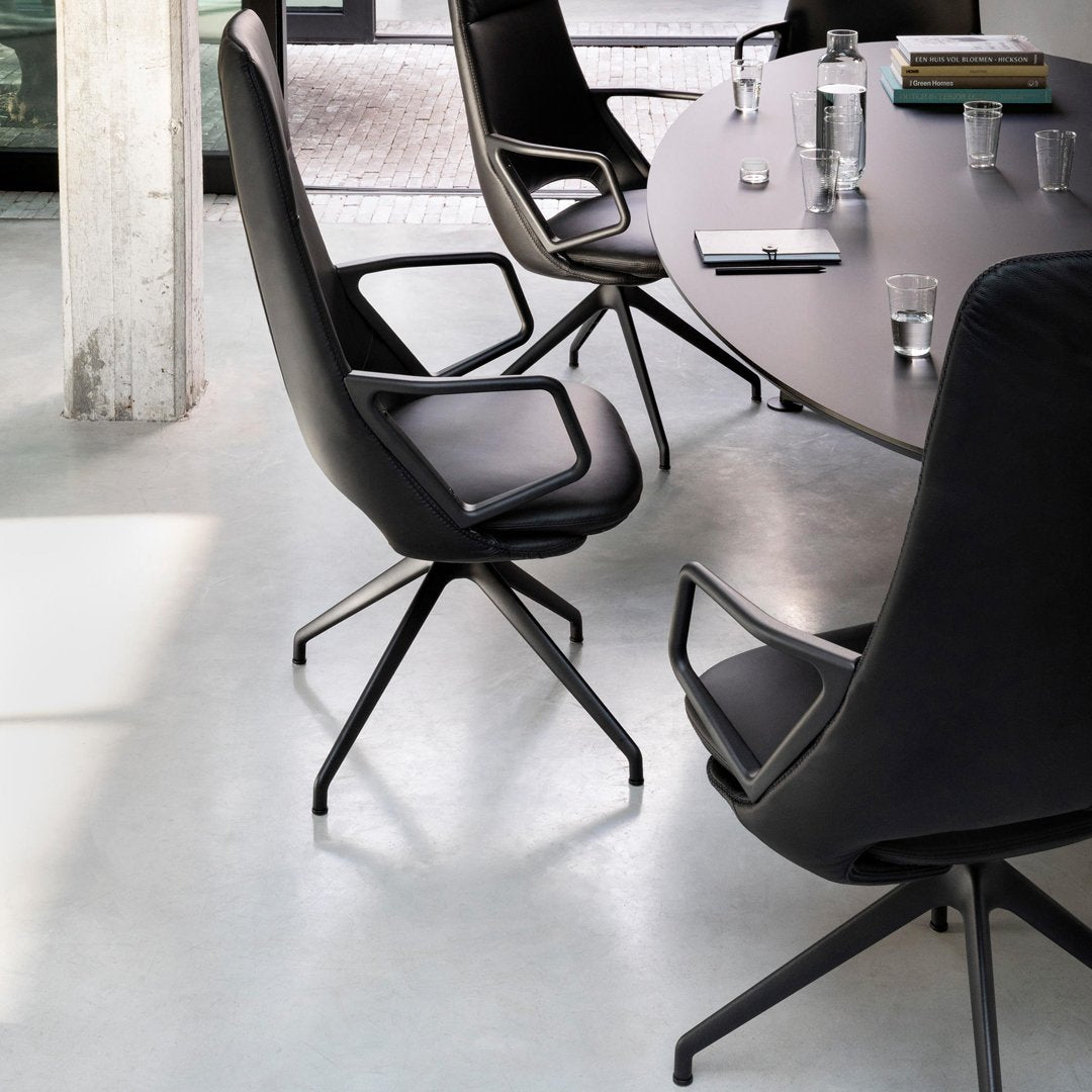Modern black swivel chair with sleek curves and minimalist design, set against a light gray floor and round dark table.